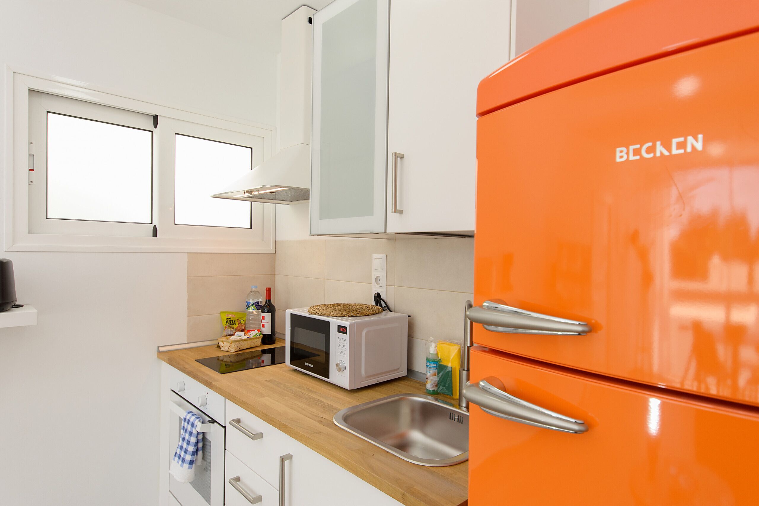 A kitchen with white cabinets, a wooden countertop, a microwave, a sink, and an orange refrigerator.
