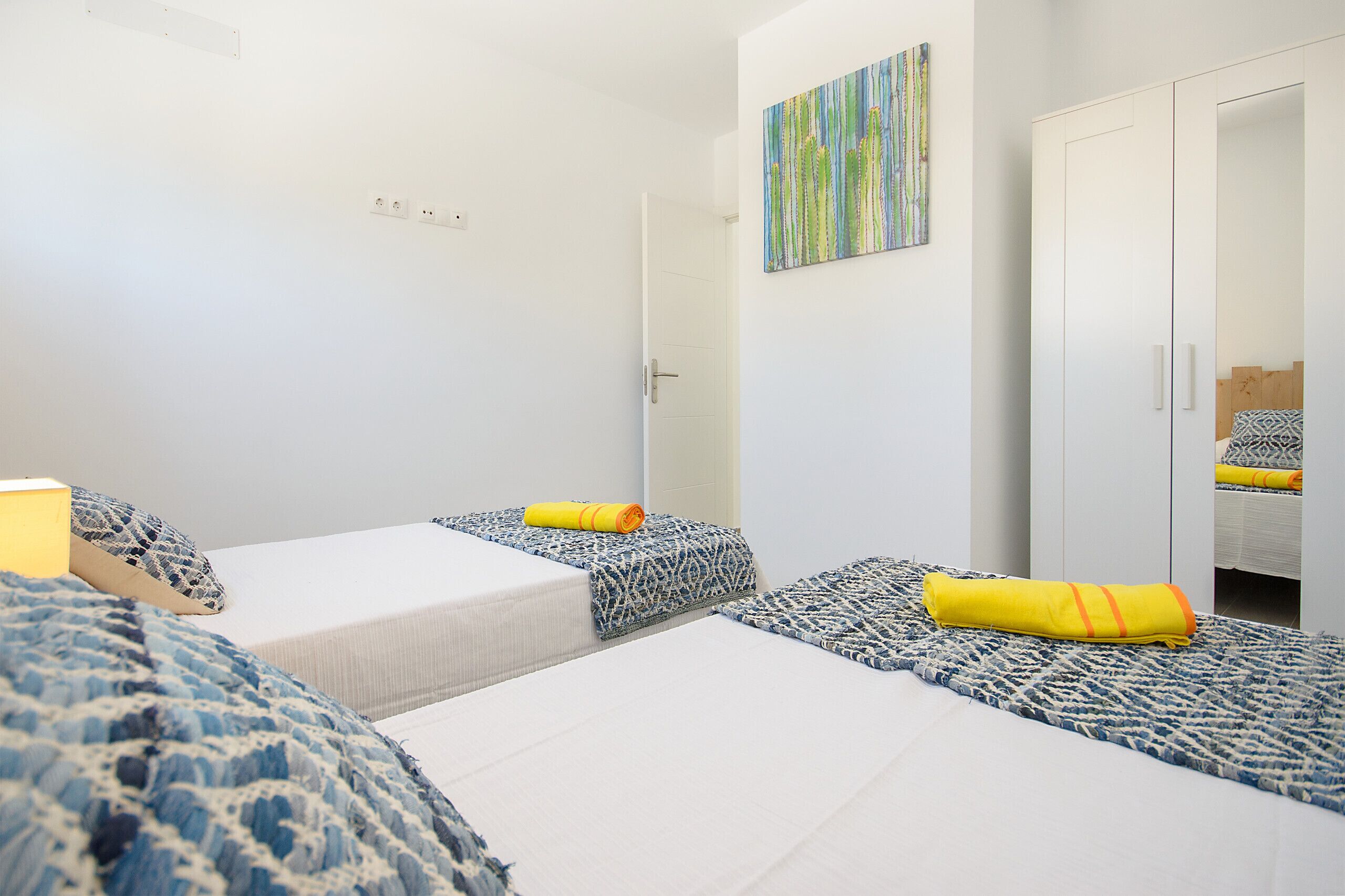 A room with two beds, a wardrobe, and a door leading to another room.