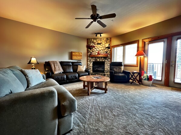 A cozy living room with a fireplace, leather sofa, and a ceiling fan. - Alpine Retreat: 2BR Ski-In/Ski-Out Condo with Private Hot Tub (Kimberley)