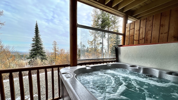 Un bain à remous avec une terrasse en bois et une vue sur une forêt et des montagnes.