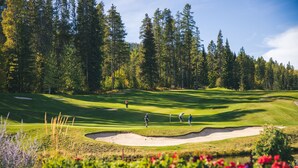 Un parcours de golf avec des bunkers de sable, un étang et des arbres denses en arrière-plan.