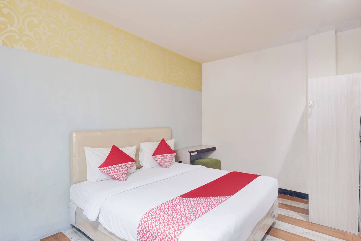 Ein ordentlich bezogenes Bett mit weißer und roter Bettwäsche, ein Nachttisch und ein Kleiderschrank in einem Hotelzimmer.