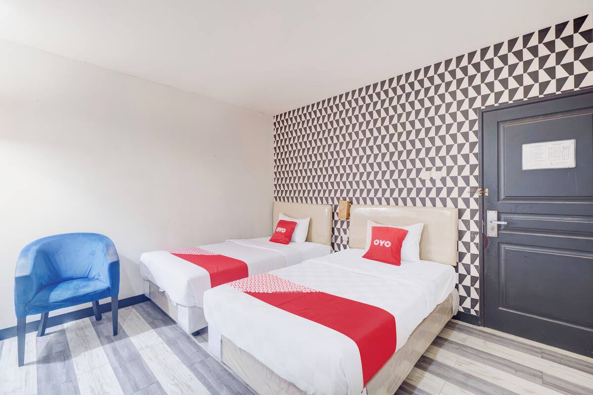 Ein Hotelzimmer mit zwei Betten, einem blauen Sessel und einer Wand mit Muster.