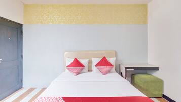 A hotel room with a bed, two pillows, a bedside table, and a green ottoman.