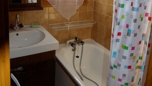 Une salle de bain avec un lavabo, un miroir, une fenêtre, une douche et un mur recouvert de carreaux.