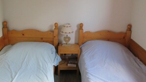 Une petite pièce simple, avec deux lits simples, des têtes de lit en bois, une table de chevet avec une lampe et un placard au-dessus des lits.