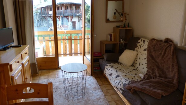 Un salon chaleureux avec un canapé, une petite table ronde et un téléviseur posé sur un meuble en bois.