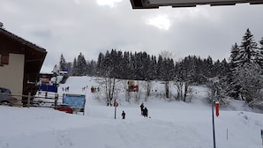 Une piste de ski enneigée avec des skieurs, un télésiège et un bâtiment portant une enseigne.