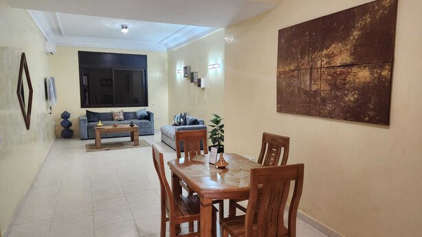 A dining area with a wooden table and chairs, a sofa, and a large abstract painting on the wall. - Résidence Belle Vue 6  (Marrakech)