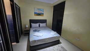 A bedroom with a bed, a nightstand, a painting, and a door. - Résidence Belle Vue 6  (Marrakech)