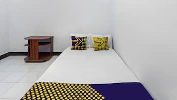 Una habitación con una cama, una mesita de madera y dos almohadas con estampado amarillo y azul.