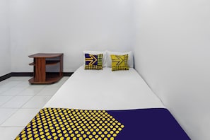 Una habitación con una cama, una mesita de madera y dos almohadas con estampado amarillo y azul.