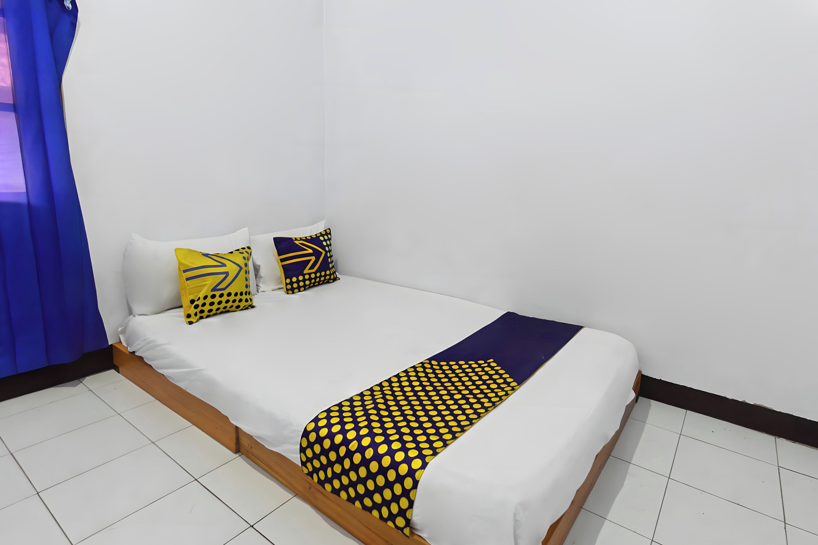 Ein Zimmer mit einem Einzelbett, Holzrahmen, weißer Bettwäsche und zwei Zierkissen.