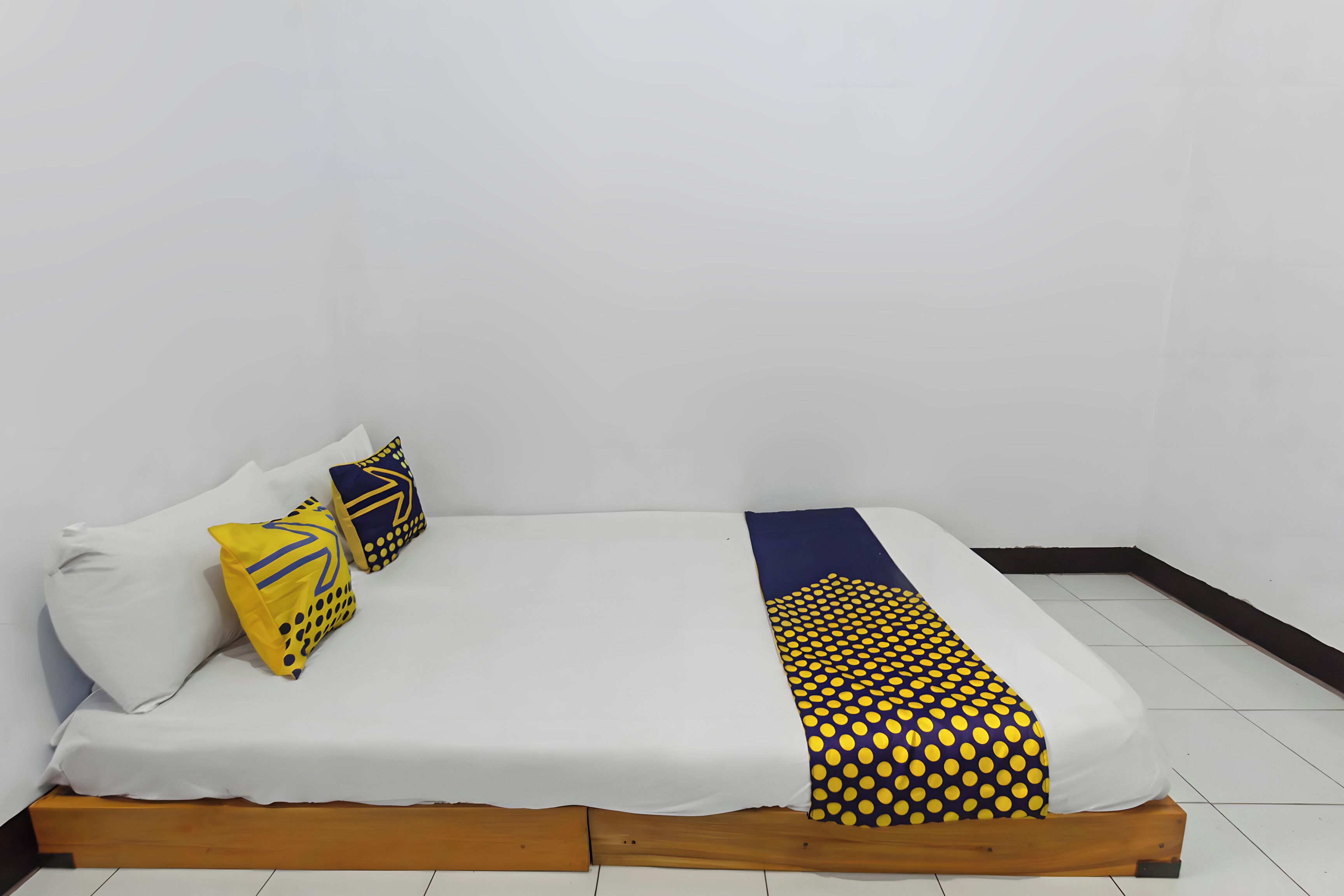 A bed with a wooden frame, white bedding, and two decorative pillows with geometric patterns.