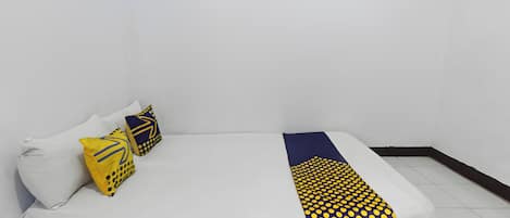 Una cama con estructura de madera, ropa de cama blanca y dos almohadas decorativas con diseños geométricos.