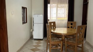 Un comedor con una mesa redonda de madera y sillas, un refrigerador blanco y una ventana con cortinas.
