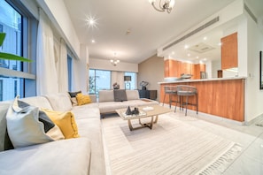 A modern living room with a sofa, coffee table, and kitchen area with wooden cabinets and bar stools.