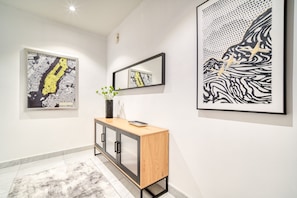A hallway with artwork on the walls, a wooden cabinet, and a mirror.
