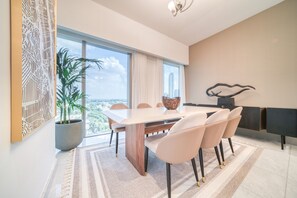 A modern dining area with a large table, six chairs, a potted plant, and a view of the city through large windows. - Modern Elegance w/ a New York Edge DIFC Apt (Dubai)