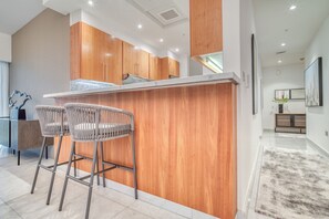 A modern kitchen with wooden cabinets, a white countertop, and two woven chairs.