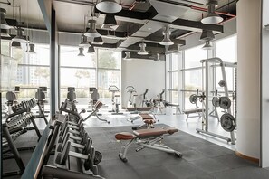 Un gimnasio moderno con diverso equipo de ejercicio, amplias ventanas y un techo alto con conductos expuestos.
