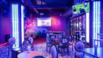 A restaurant with a large screen displaying a sports event, a mural, and a cozy seating area with tables and chairs.