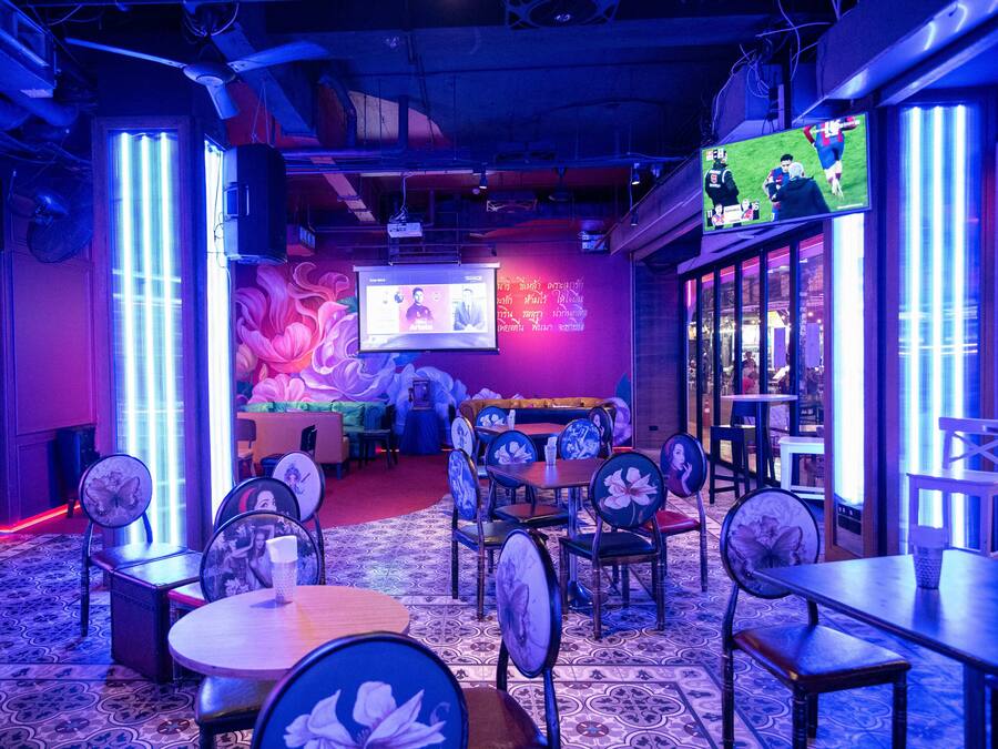 A restaurant with a large screen displaying a sports event, a mural, and a cozy seating area with tables and chairs.