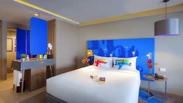 A modern hotel room with a large bed, a bedside table, a desk with a chair, and a bathroom visible through a door.