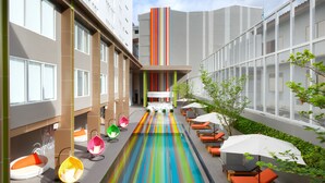 Un moderno vestíbulo de hotel con piscina central, zonas de estar y un edificio alto al fondo.