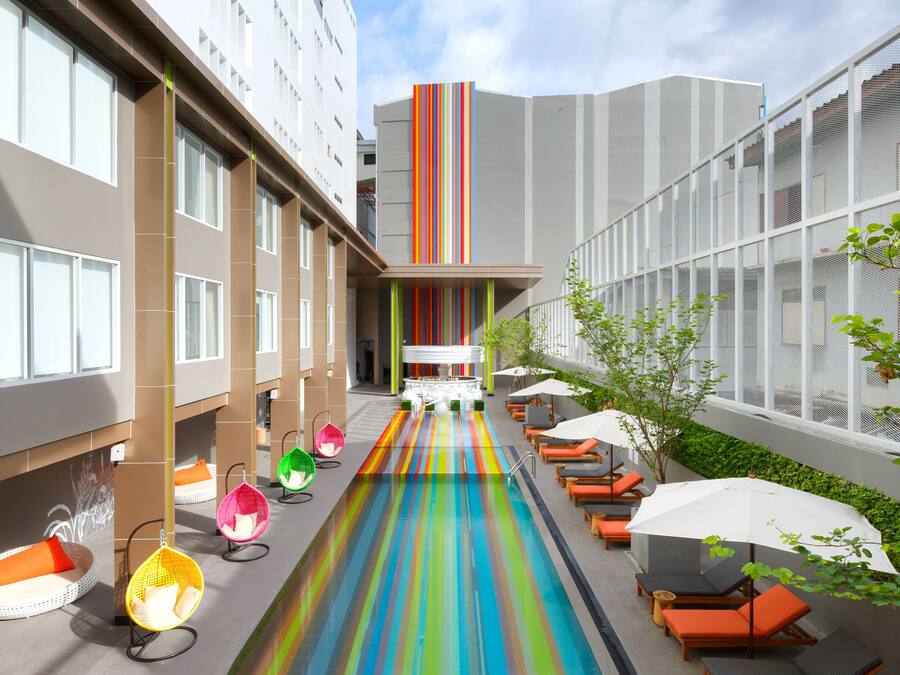 Un moderno vestíbulo de hotel con piscina central, zonas de estar y un edificio alto al fondo.