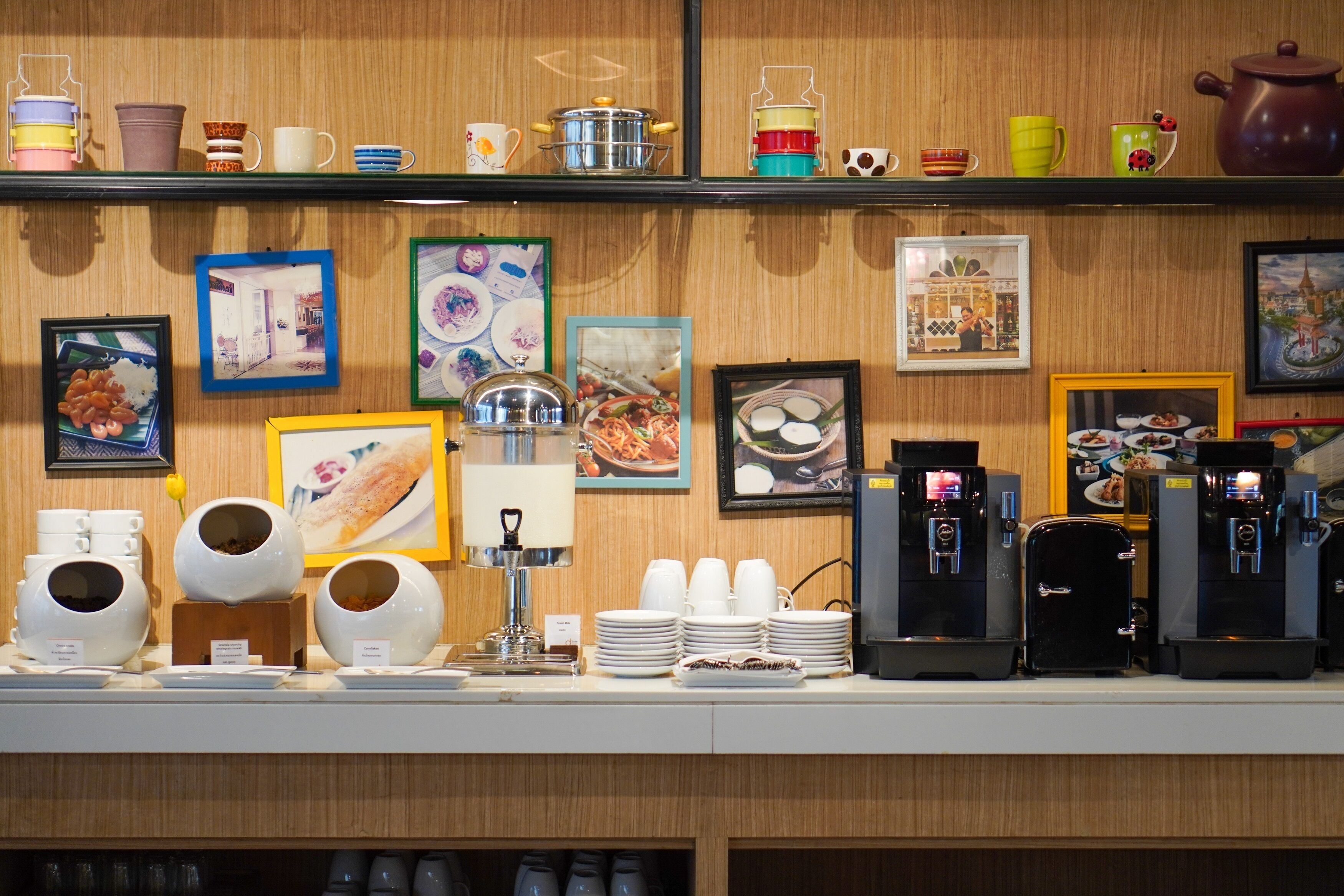 Una barra de cafetería con varias máquinas de café, una selección de tazas y vasos, y cuadros en la pared.
