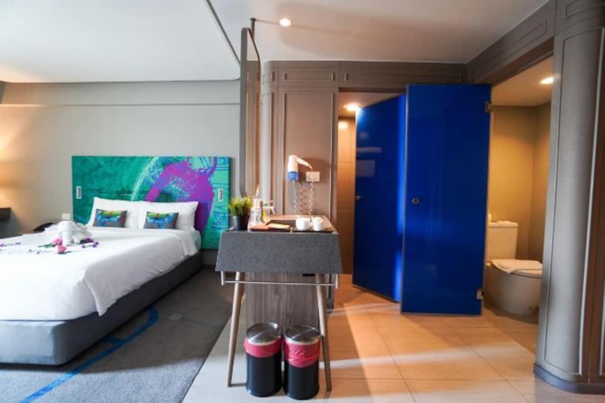 Habitación de hotel con cama, mesita de noche y baño con puerta azul.