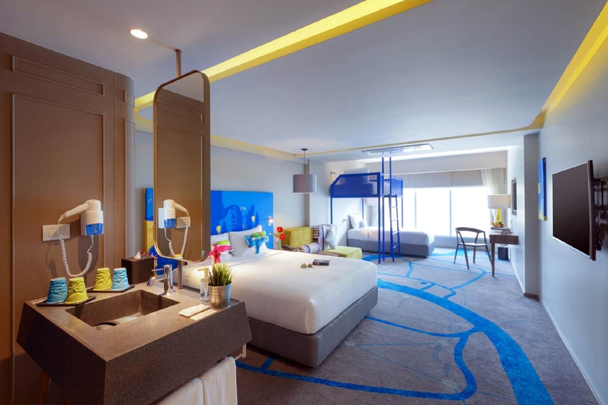 A modern hotel room with a large bed, a built-in vanity, and a large mirror.