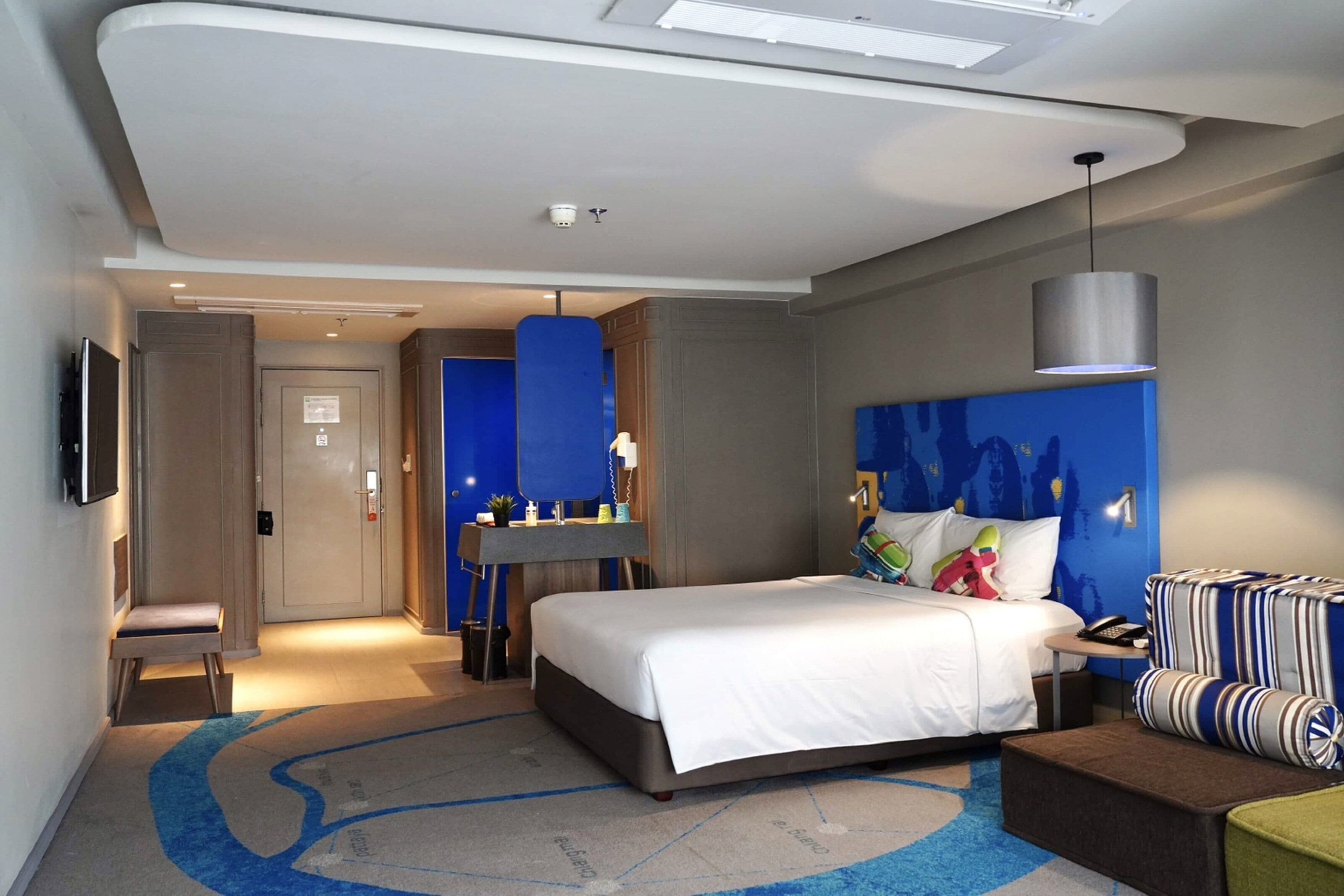 A modern hotel room with a large bed, a desk, a chair, and a sofa.