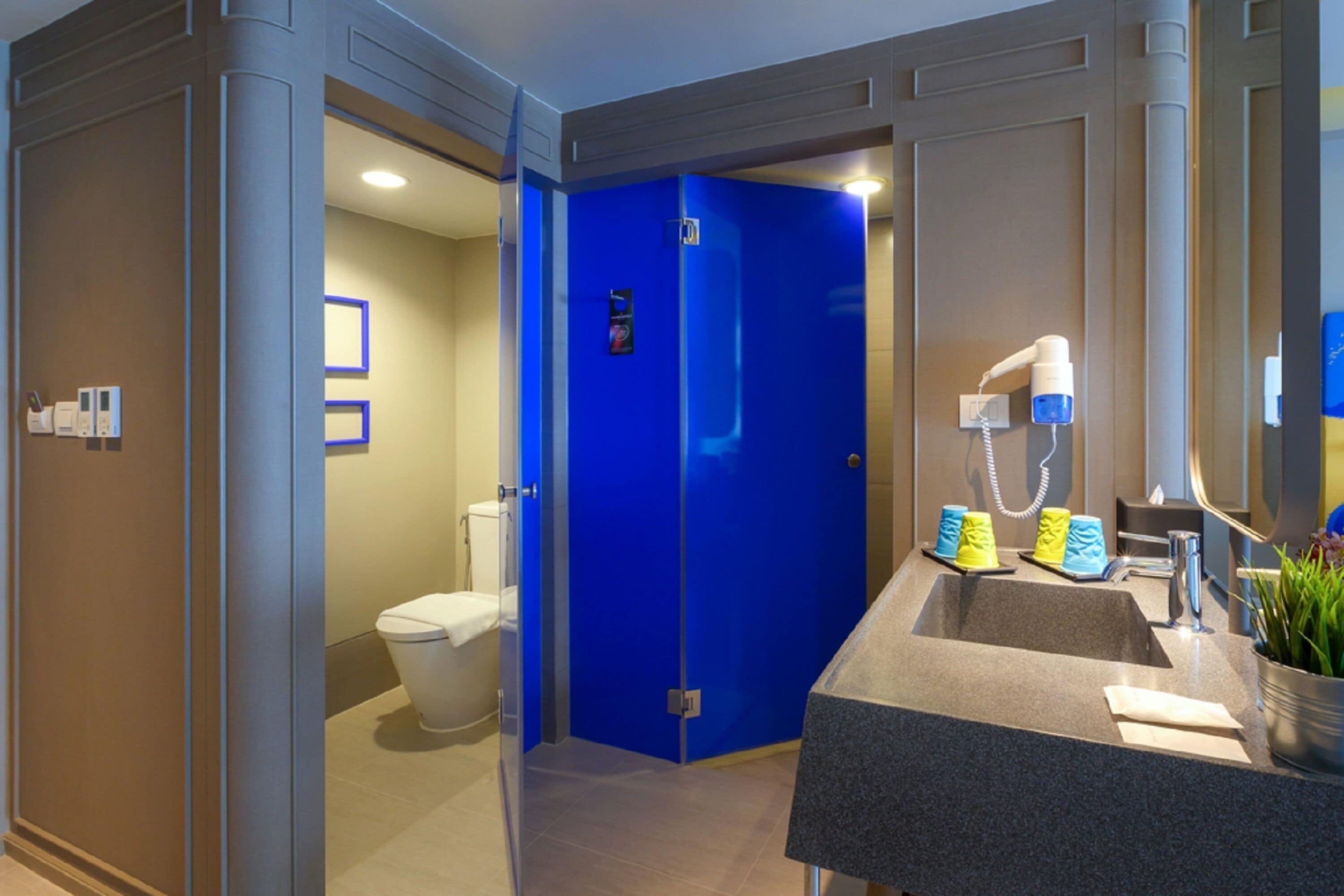 A modern bathroom with a blue door, a sink with a mirror, and a toilet.