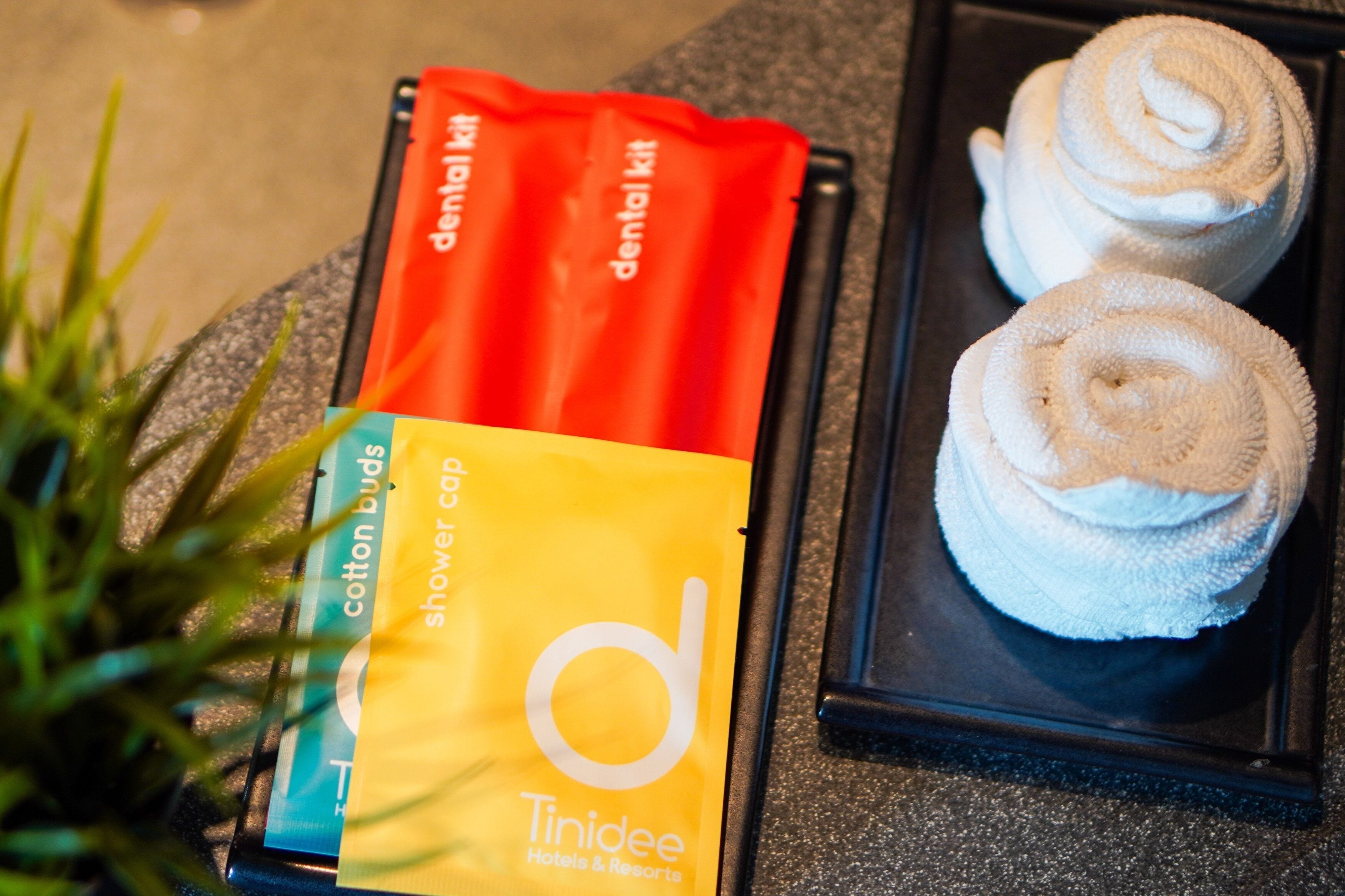 A bathroom with a towel rack holding two white towels, a red dental kit, and a yellow shower cap.