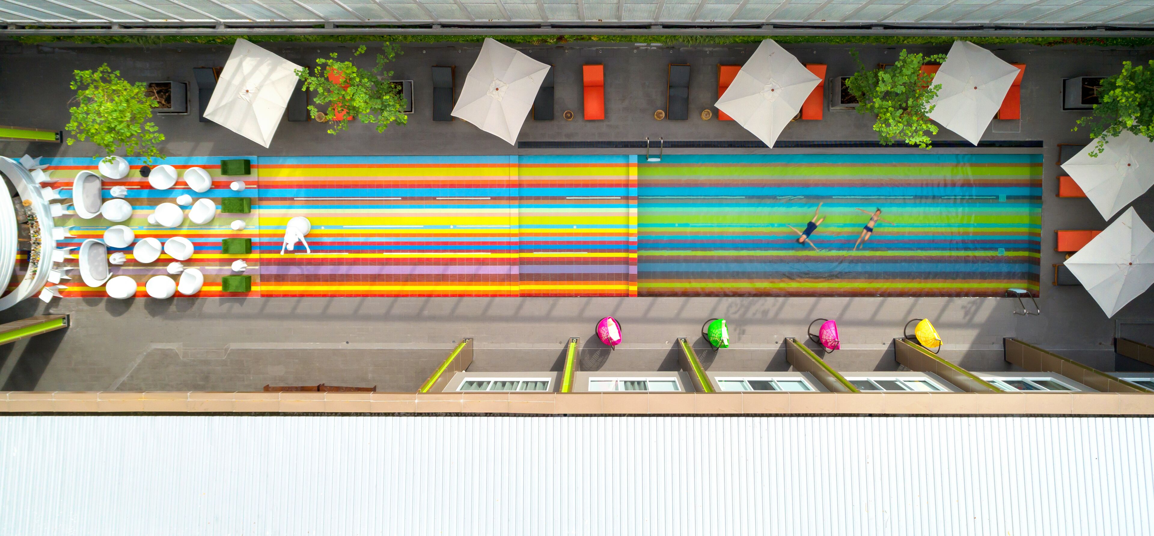 Una piscina sul tetto con un design colorato a righe, diversi ombrelloni e zone relax.