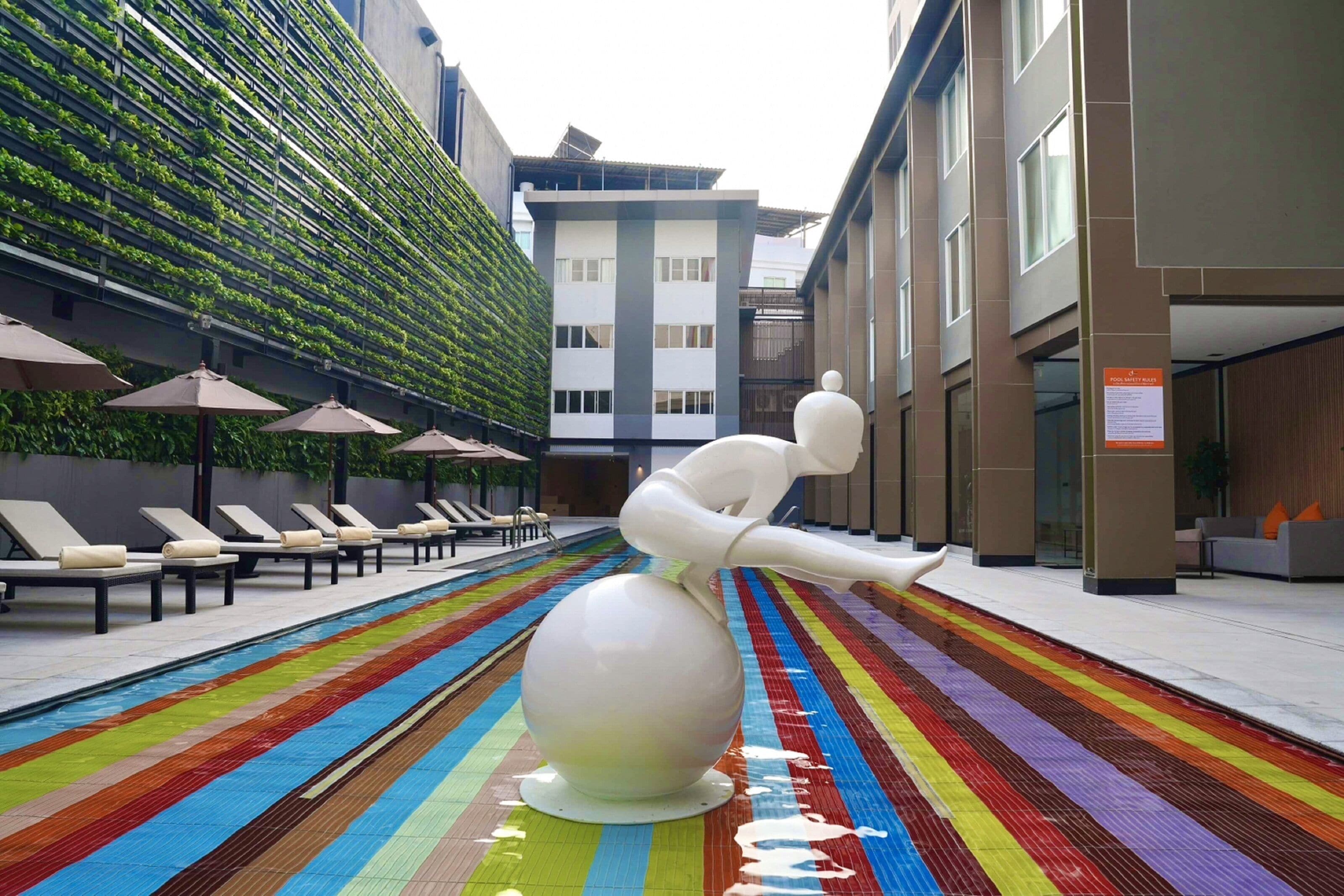 A swimming pool with a colorful striped floor, lounge chairs, and a white sculpture.