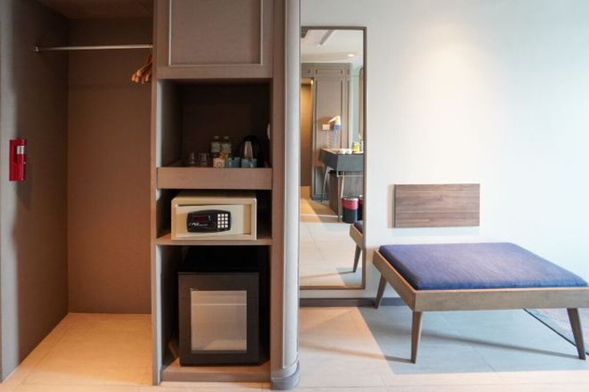 Una habitación de hotel moderna con armario empotrado, un pequeño rincón de descanso y un espejo que refleja la habitación.