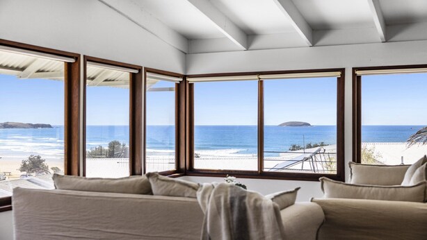 A room with large windows offering a view of the ocean and a beach. - Victoria's - Hamptons Charm, Pool, Pizza Oven, Spectacular Ocean Views (Emerald Beach)