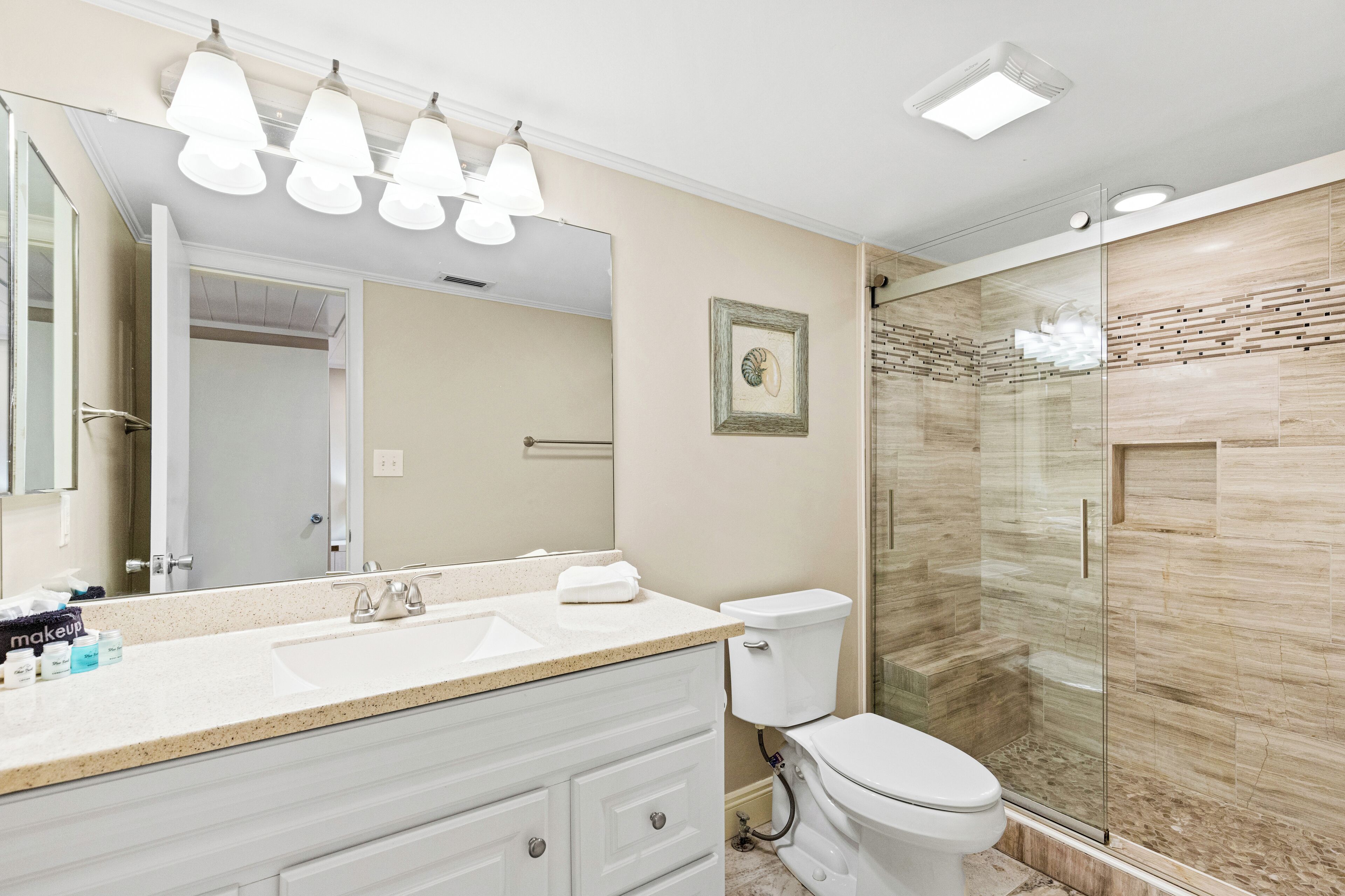 A modern bathroom with a large mirror, a sink, a toilet, and a glass-enclosed shower.
