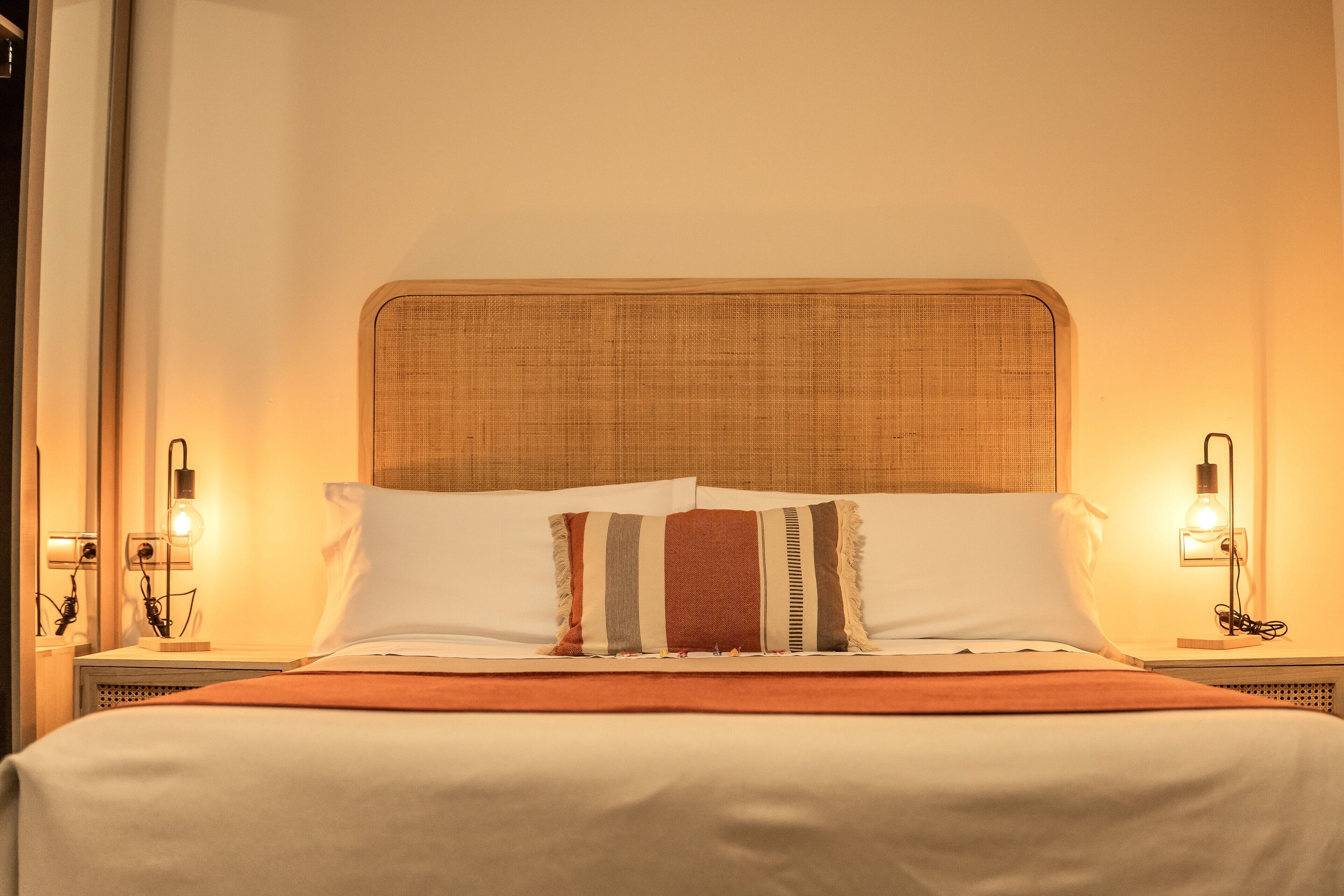 Una cama bien hecha con un cojín a rayas, un cabecero de madera y lámparas de noche.