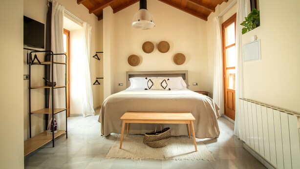 A bedroom with a bed, a wooden bench, a hanging light fixture, a TV, and a shelf with a basket. - APARTAMENTOS VITA CENTER  (Granada)