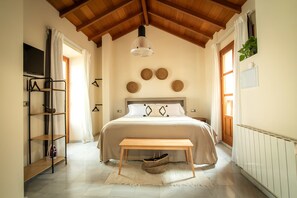 A bedroom with a bed, a wooden bench, a hanging light fixture, a TV, and a shelf with a basket. - APARTAMENTOS VITA CENTER  (Granada)