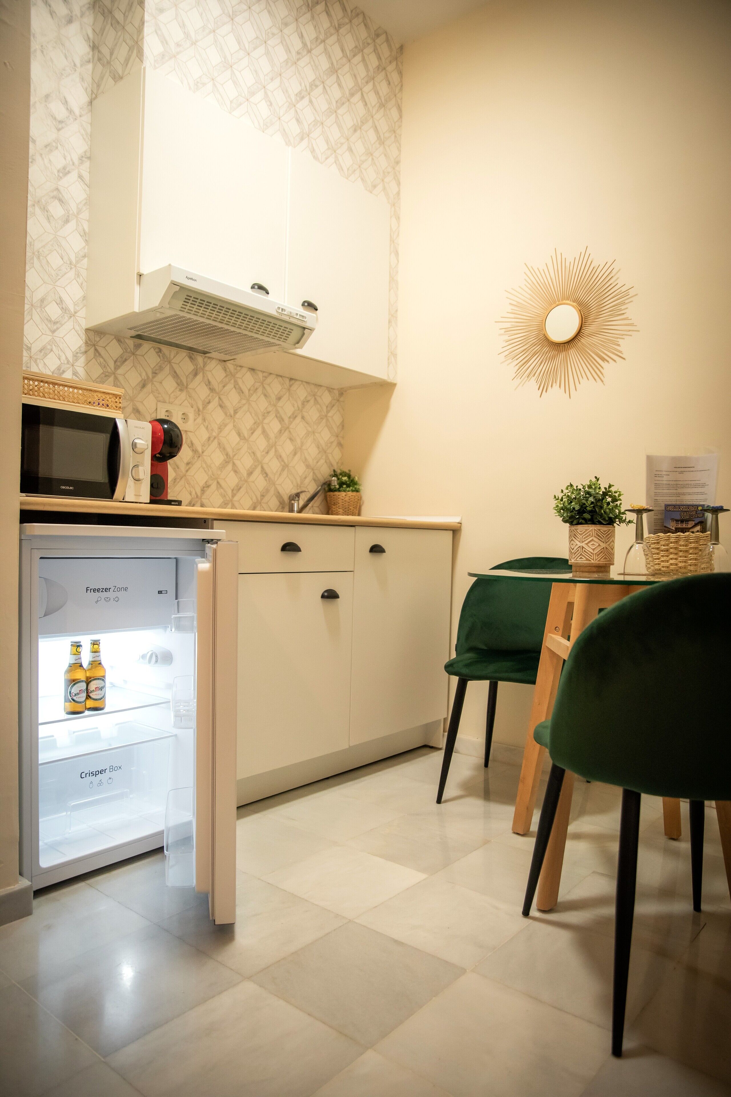 A compact kitchen with a refrigerator, microwave, and a small dining area with a green chair and table.
