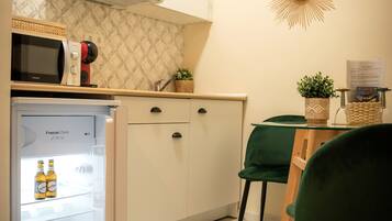 Una cocina compacta con refrigerador, microondas y un pequeño comedor con una silla y una mesa verdes.