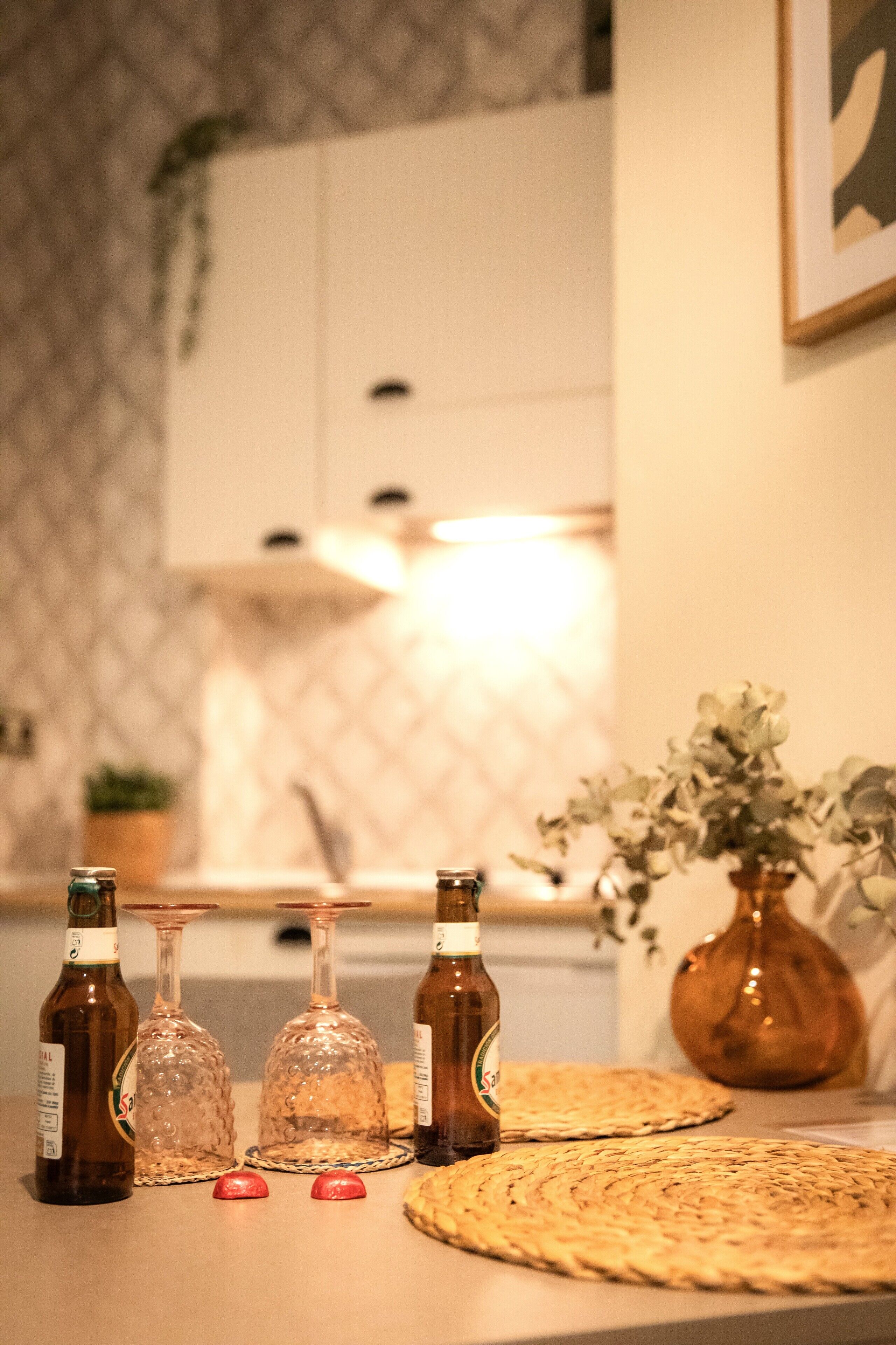 En köksbänk med flaskor, glas och vävda bordsunderlägg.