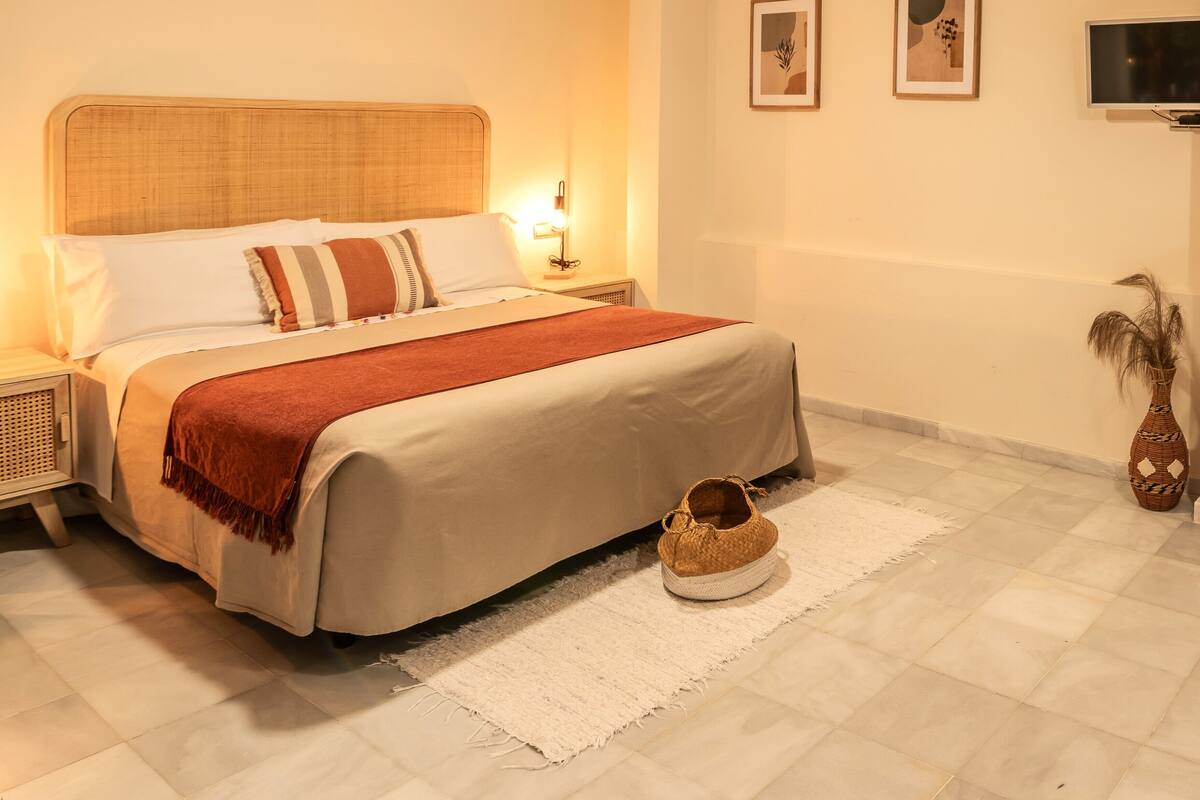 A neatly arranged bedroom with a bed, bedside tables, a TV, and a decorative vase.