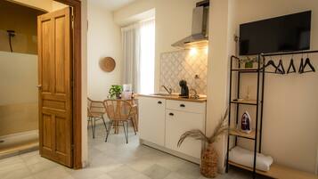 Una cocina compacta con comedor, una puerta de madera, un televisor montado en la pared y un estante con objetos colgando.