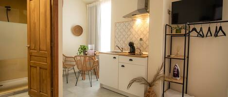 A compact kitchen with a dining area, a wooden door, a TV mounted on the wall, and a shelf with hanging items.